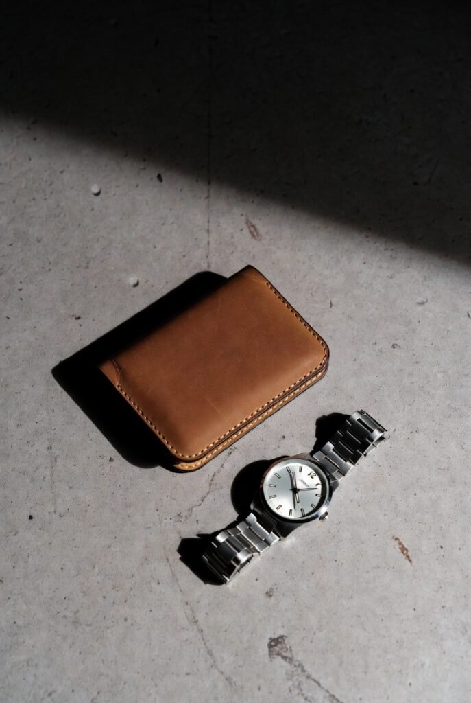 High-quality leather wallet and steel watch on concrete — subtle marks only, no giant logos.