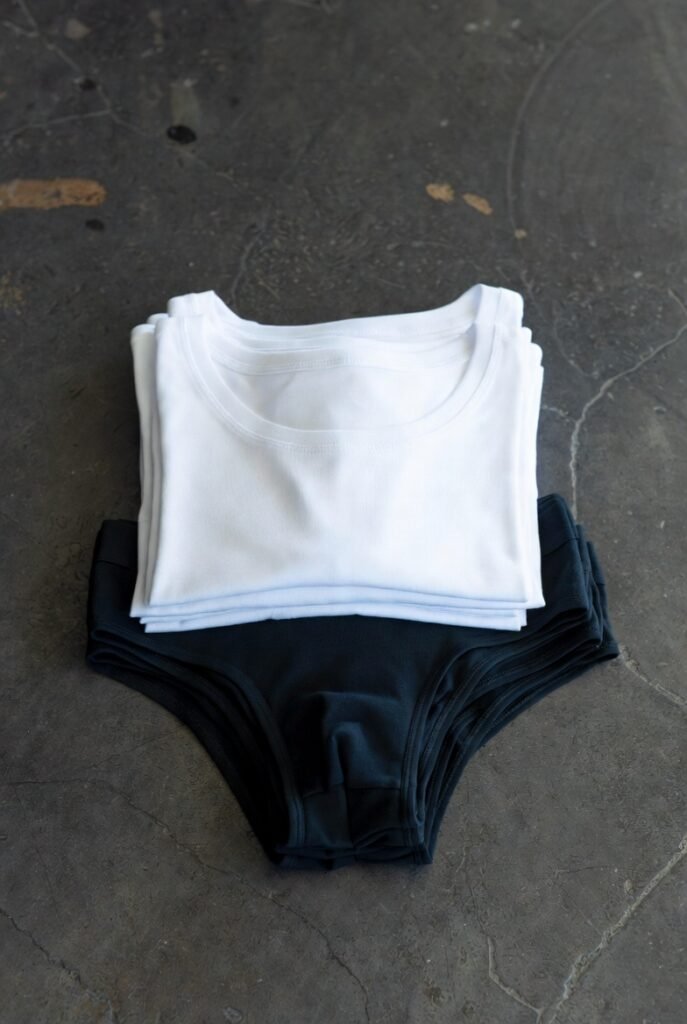 Stack of plain white undershirts and black briefs on dark concrete — foundation matters