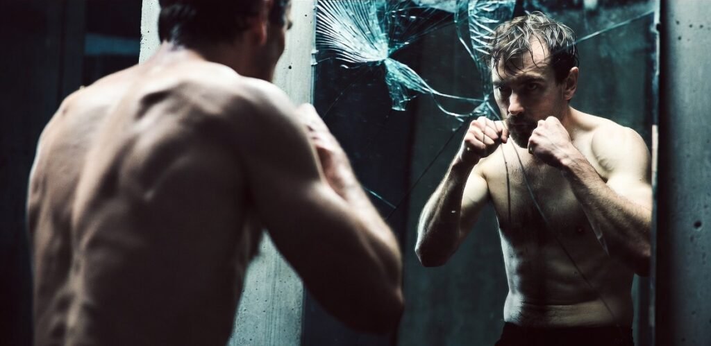 Rugged man in gritty concrete setting intensely training his mindset through shadow boxing or focused reflection. Dark moody high-contrast photography embodying masculine mental toughness, discipline, and grit. No fluff — pure signal.